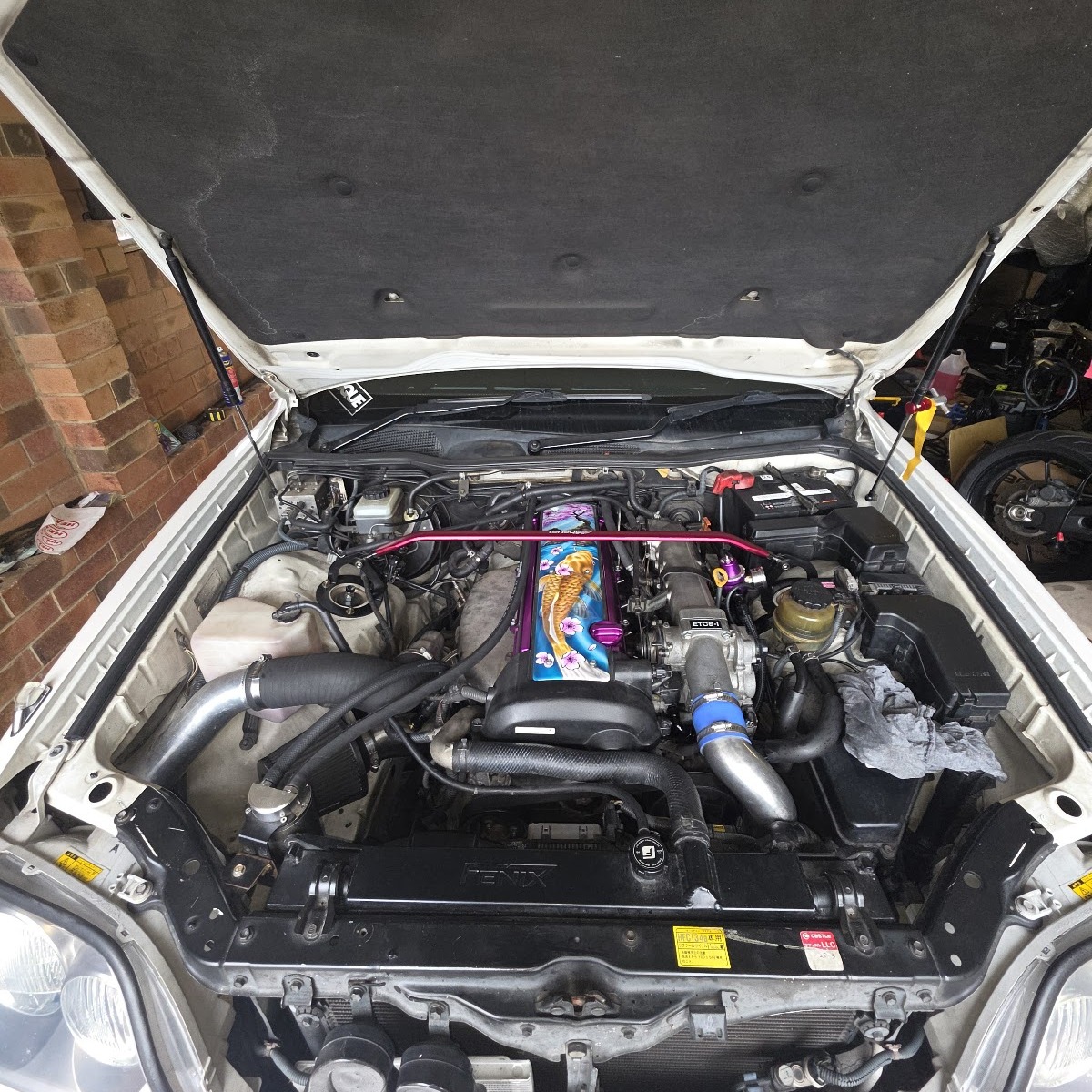 A finished engine bay with custom pipework and a painted coil cover